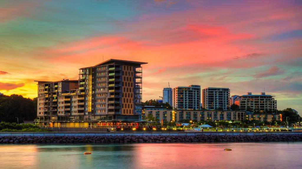 a city skyline at sunset with buildings and the water at Darwin Waterfront Luxury Suites in Darwin