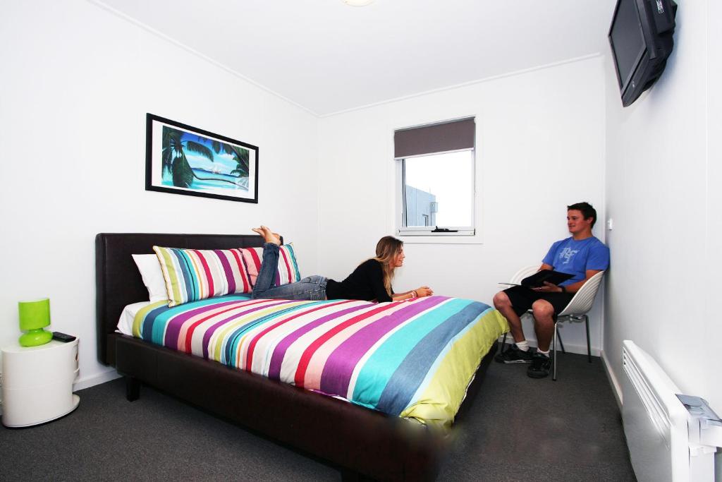 Ein Mann und eine Frau sitzen auf einem Bett in einem Zimmer in der Unterkunft The Island Accommodation in Phillip Island