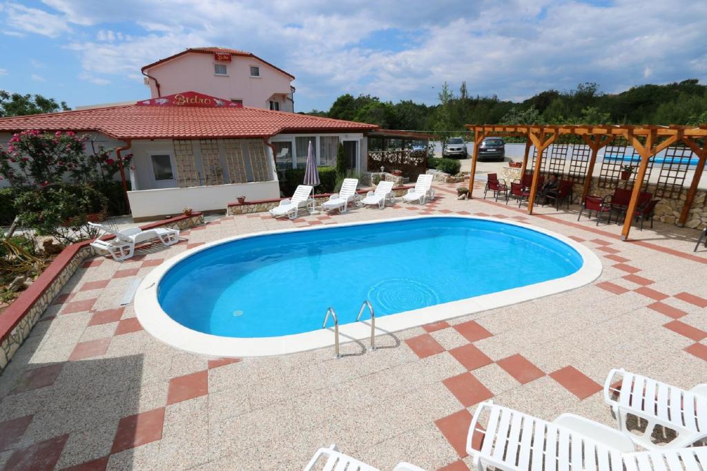 a swimming pool with chairs and a house at Pansion Comfort Sidro in Novalja