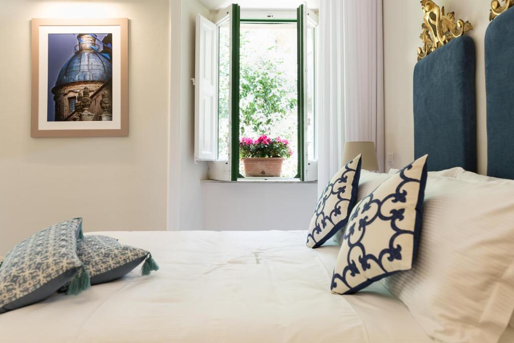 Un dormitorio con una cama blanca con almohadas y una ventana. en Palazzo Taranto Luxury Rooms, en Caltagirone