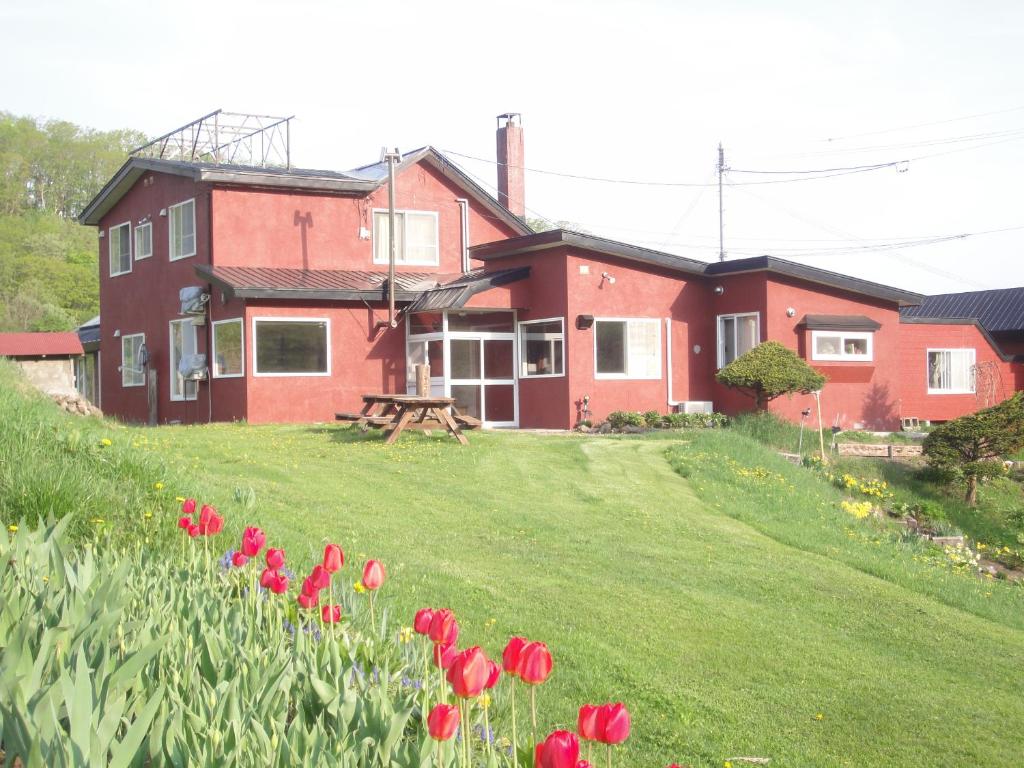 dom z czerwonymi kwiatami przed nim w obiekcie Farm Inn Anima no Sato w mieście Abashiri