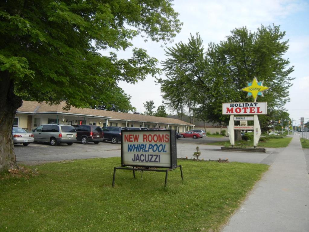 un cartel en el césped frente a un motel en Holiday Motel, en Orillia