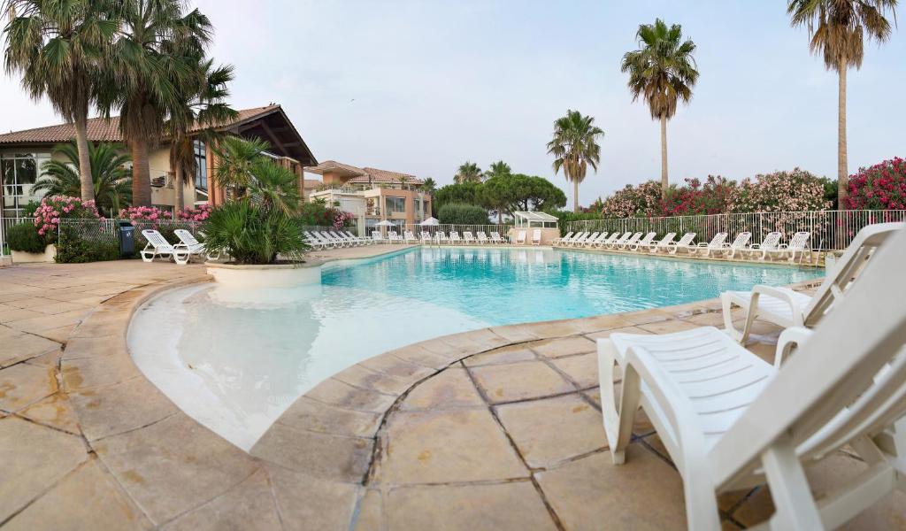 une grande piscine avec des chaises blanches et des palmiers dans l'établissement Residence Cap Hermes - maeva Home, à Fréjus