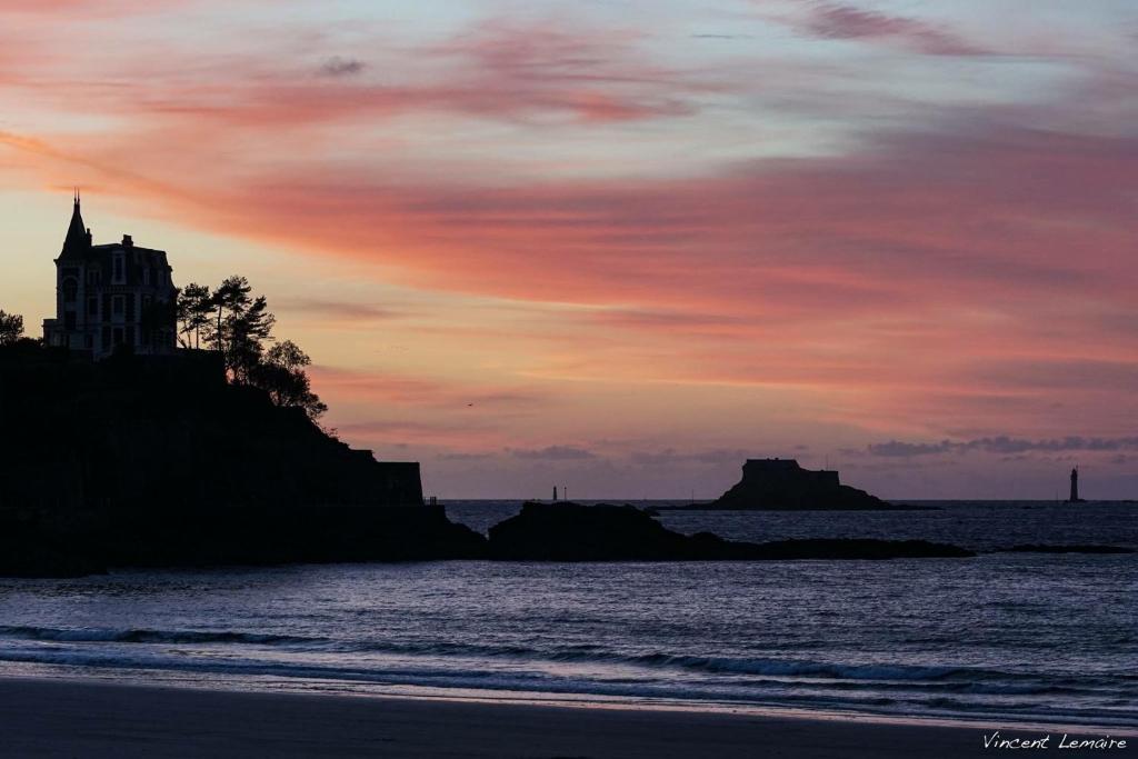 a sunset over a beach with a building on a cliff at Hôtel De La Vallée in Dinard