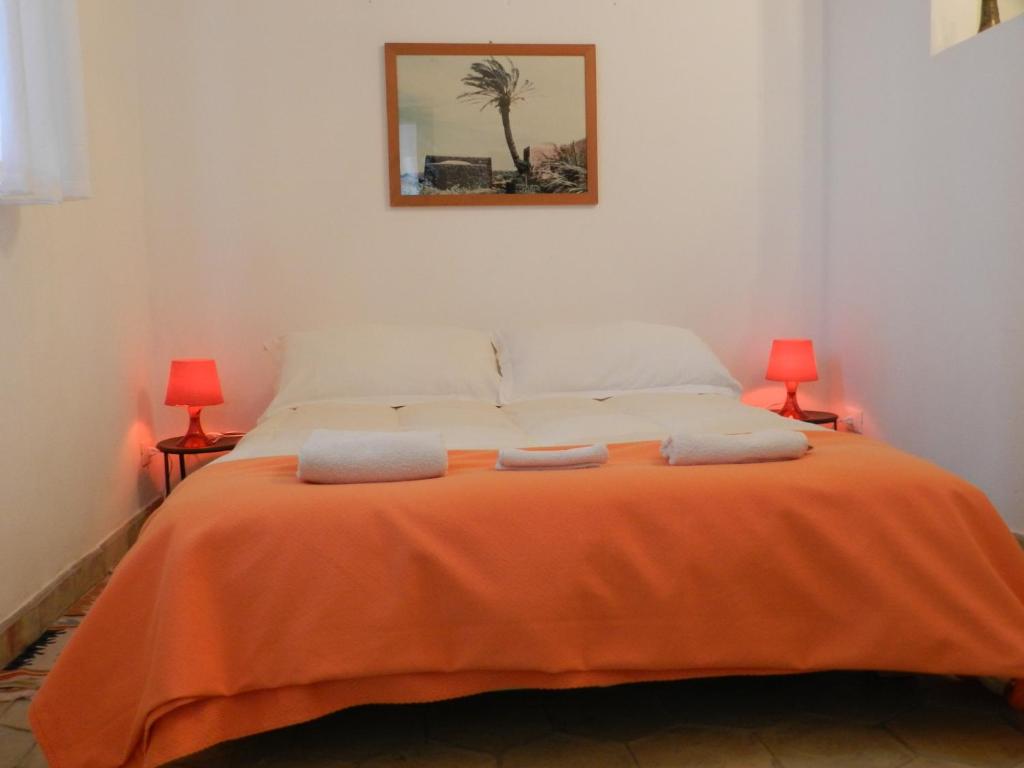 a bedroom with a bed with orange blanket and two lamps at Masseria Acque Di Palermo in Roccapalumba