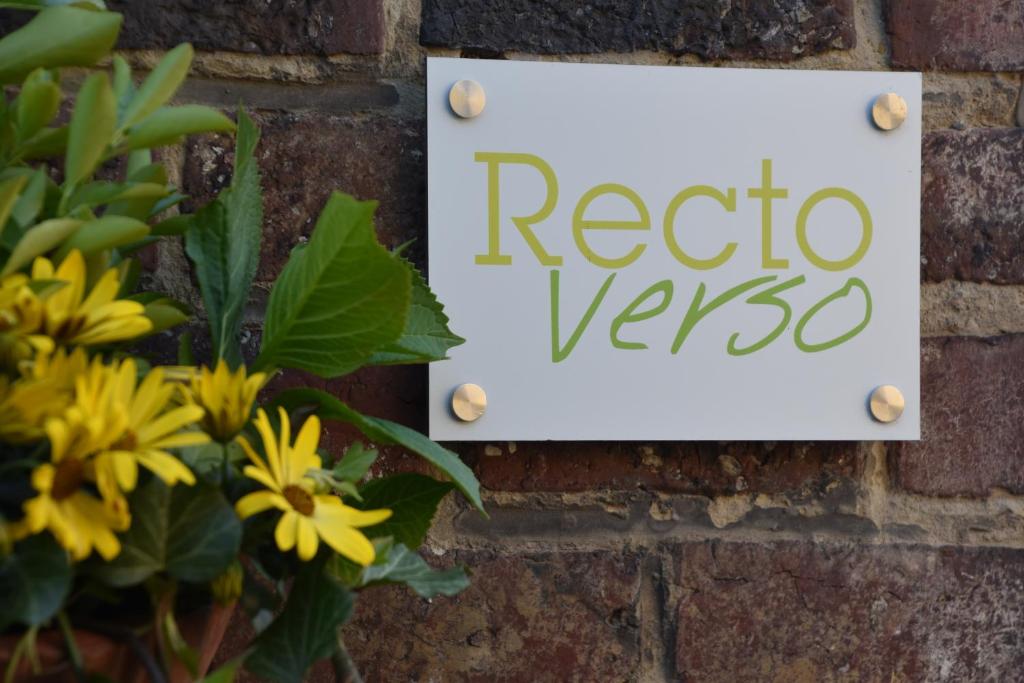 ein Schild an einer Ziegelwand mit gelben Blumen in der Unterkunft RectoVersoVV in Sint-Pieters-Leeuw
