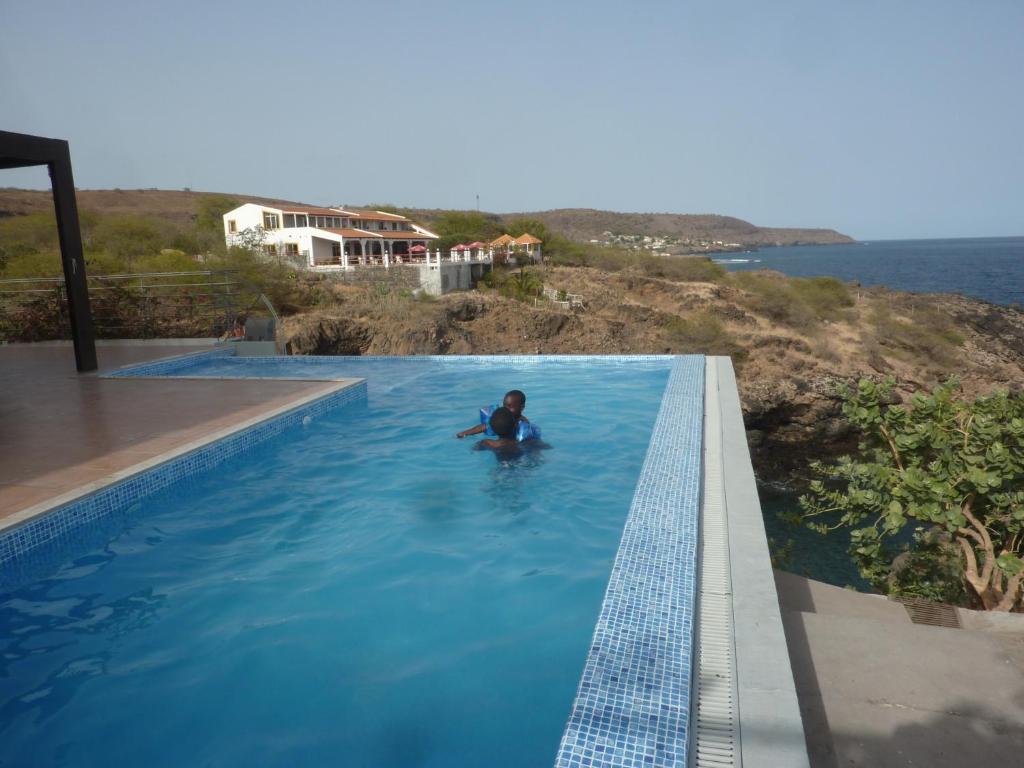 a person sitting in a swimming pool next to the ocean at Villa Halcyon Caboverde in Cidade Velha