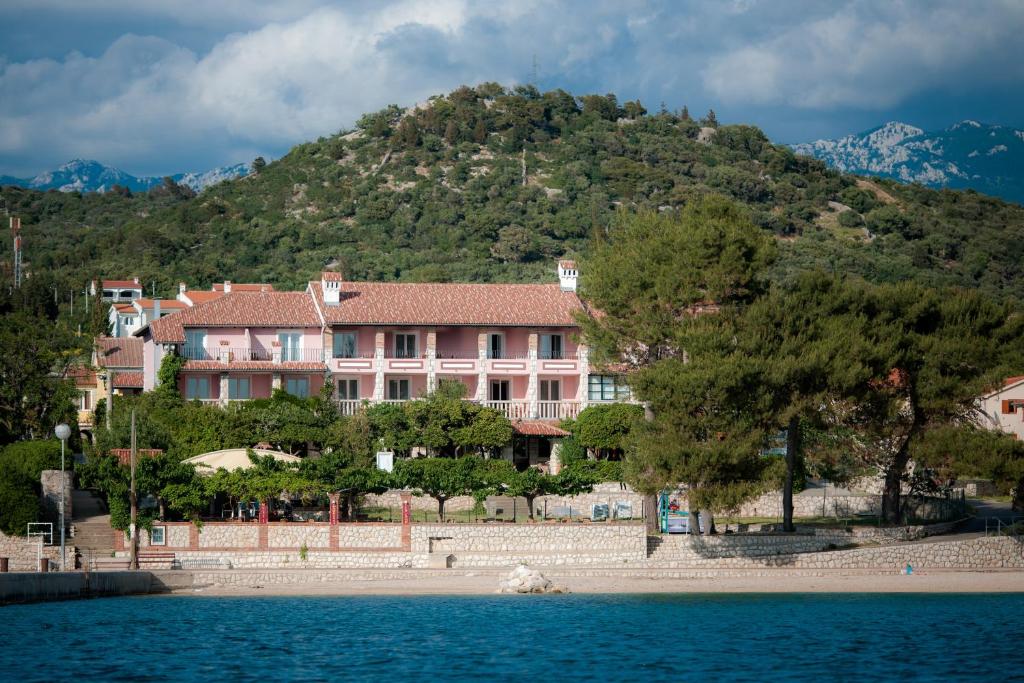 un gran edificio rosa en una colina junto a un cuerpo de agua en Hotel Villa Barbat, en Rab