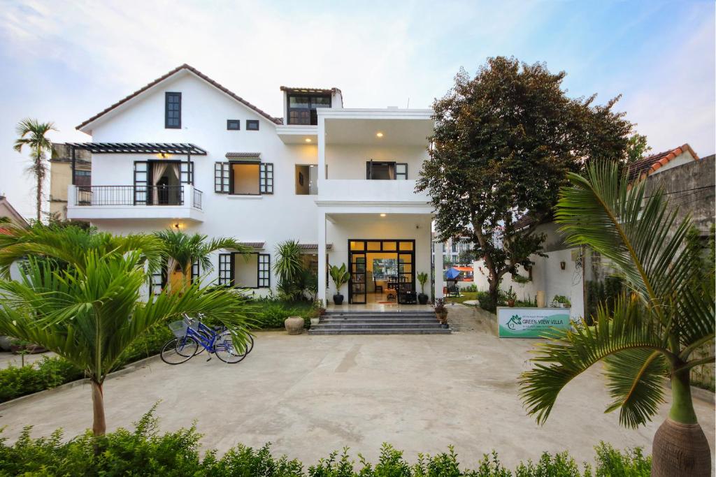 uma casa branca com palmeiras em frente em Hoi An Green View Homestay & Villa em Hoi An