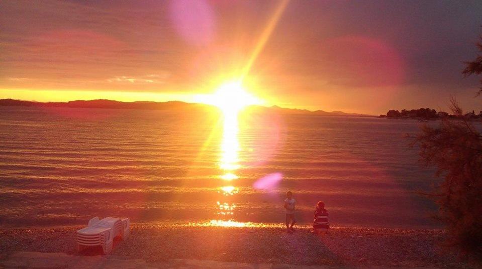 twee mensen die op het strand staan te kijken naar de zonsondergang bij Apartments Stjepic in Sukošan