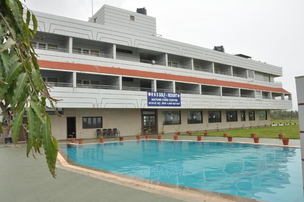 een groot gebouw met een zwembad ervoor bij RNS Golf Resort & Nature Cure Centre in Māvalli