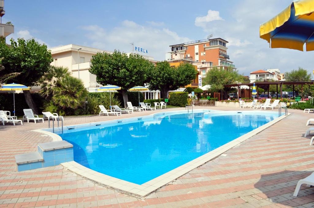 uma grande piscina com cadeiras e guarda-sóis num hotel em Hotel Perla em Senigallia
