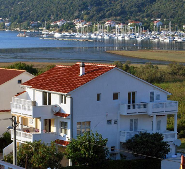 a white house with a red roof next to a harbor at Apartmani Franciska in Rab