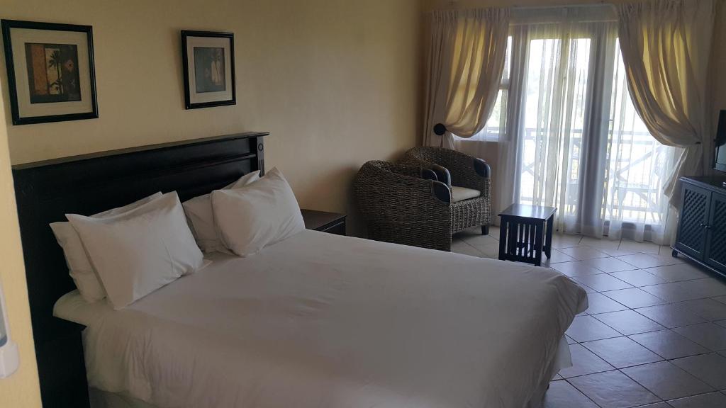 1 dormitorio con cama blanca, silla y ventana en Ocean View Villas C10, en Port Edward