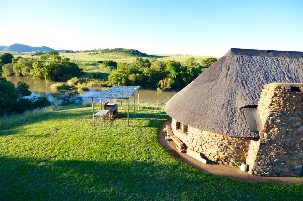 a stone building with a thatch roof on a field at Swartkop Cottage in Winterton