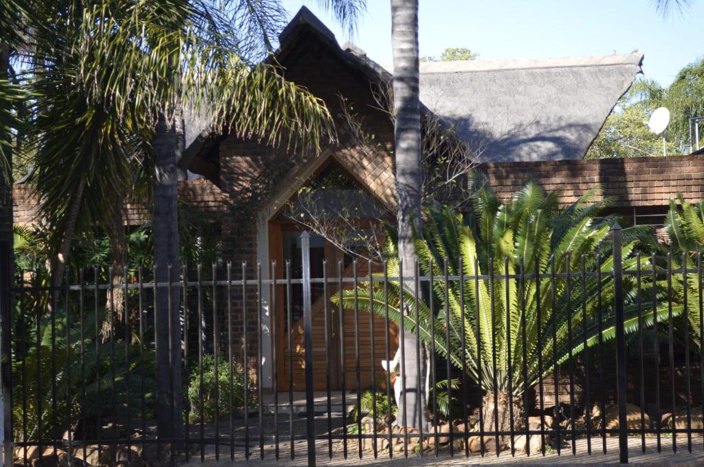 a fence in front of a house with palm trees at Birrea Guest house in Polokwane