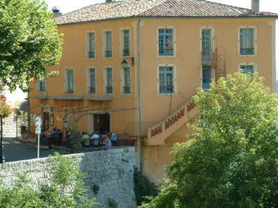 a large yellow building with people sitting outside of it at Hotel le Belvédère in Moustiers-Sainte-Marie