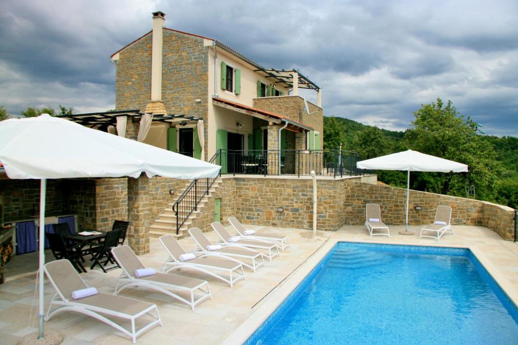a pool with chairs and umbrellas next to a house at Villa Banic in Bartolići