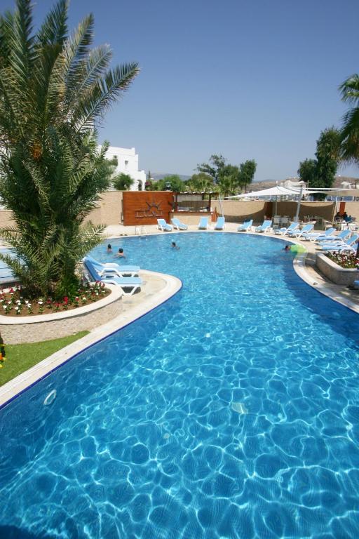 a large blue swimming pool with chairs and a palm tree at Costa Luvi Hotel Bodrum - All Inclusive in Gümbet