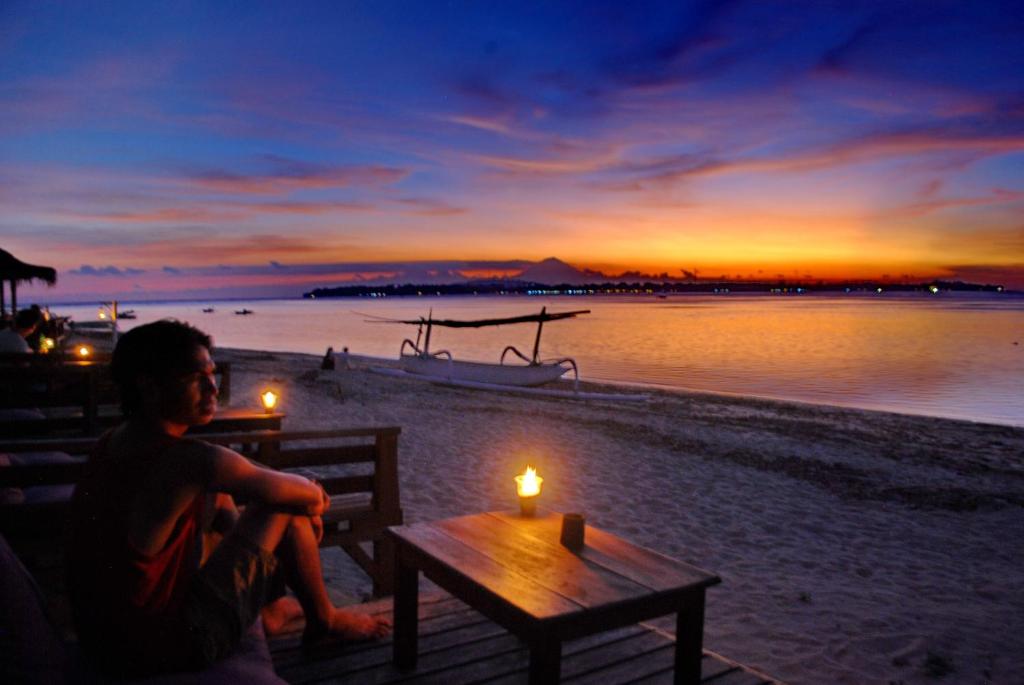 un hombre sentado en un banco viendo la puesta de sol en Matahari Bungalow 3, en Gili Air