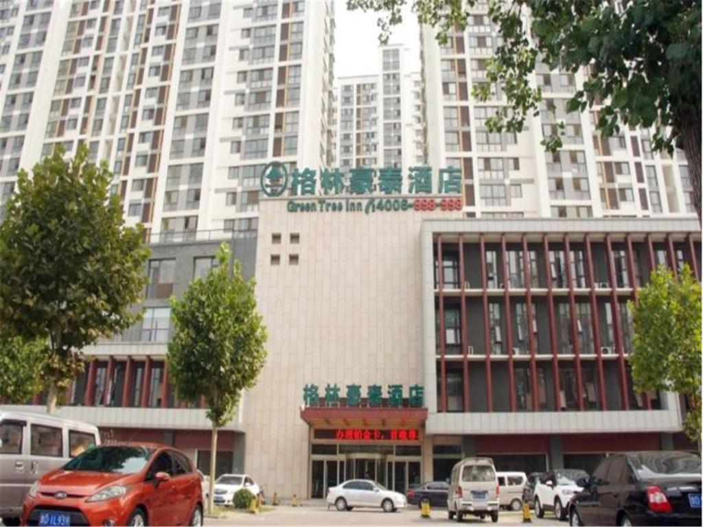 a large building with cars parked in front of it at GreenTree Inn ShanDong ZaoZhuang TengZhou FuQian Road LongQuan Square Business Hotel in Tengzhou