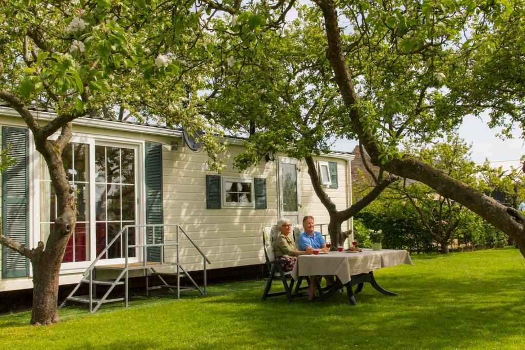 two people sitting at a table in front of a house at Minicamping de Boshoek in Serooskerke