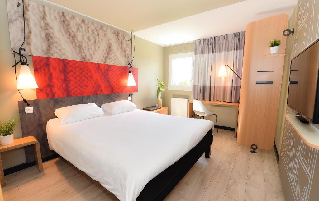 een hotelkamer met een groot bed en een televisie bij ibis Beaune La Ferme Aux Vins in Beaune