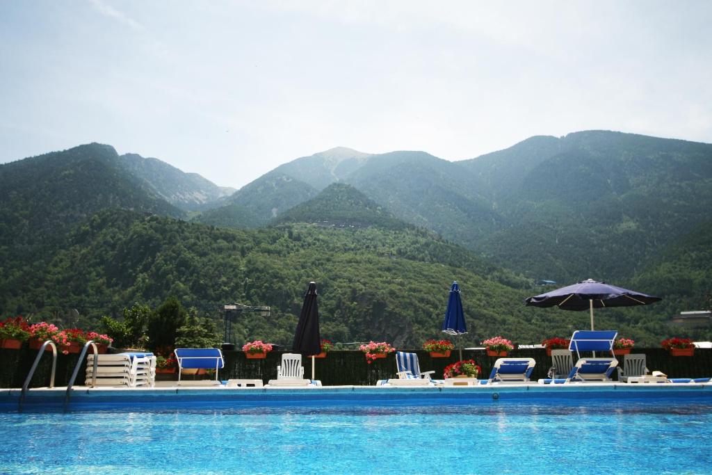 a pool with chairs and umbrellas with mountains in the background at Hotel Pyrénées in Andorra la Vella