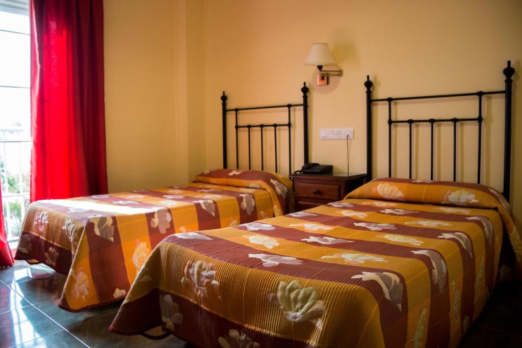 2 camas en una habitación con cortinas rojas en Hostal Restaurante La Curva, en Adra