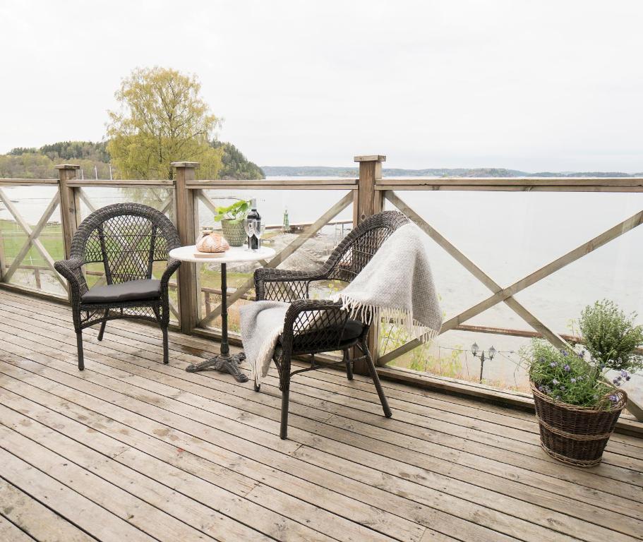 a deck with three chairs and a table and a view of the water at Anfasteröd Gårdsvik - Badstugorna in Ljungskile