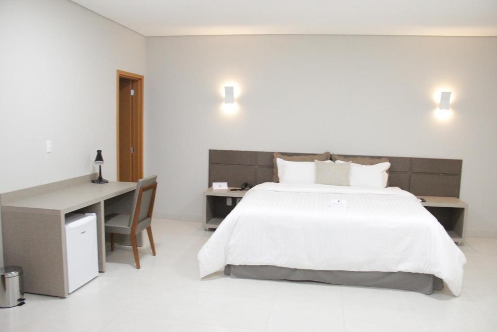 1 dormitorio con 1 cama blanca grande y escritorio en Gran Park Hotel e Convenções, en Mineiros
