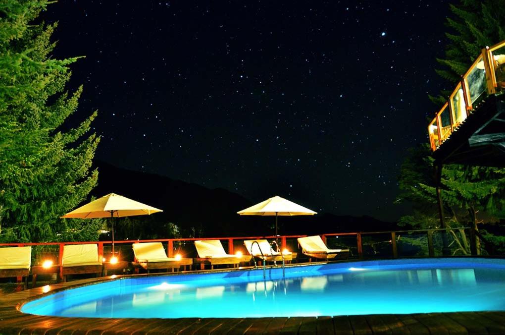 a swimming pool with chairs and umbrellas at night at Dos Bahias Lake Resort in Villa La Angostura
