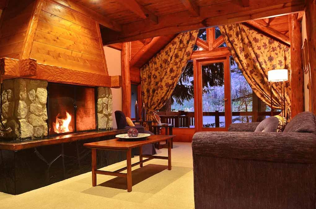 a living room with a fireplace and a couch and a table at Dos Bahias Lake Resort in Villa La Angostura