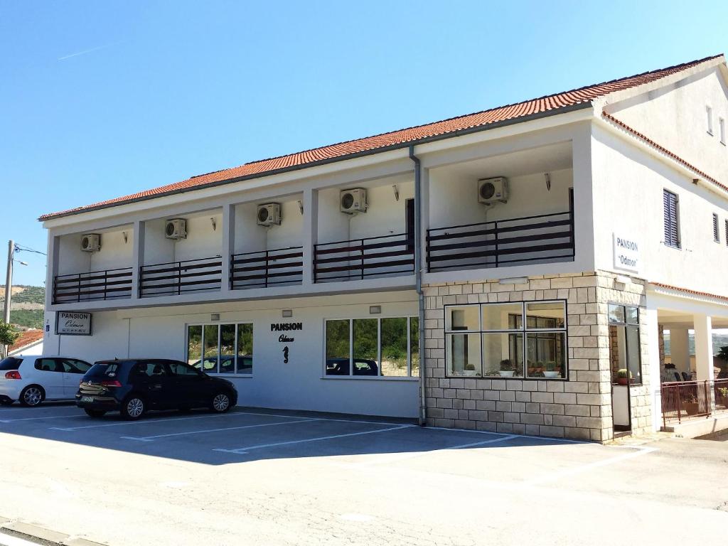 un bâtiment blanc avec des voitures garées dans un parking dans l'établissement Rooms & Pansion Odmor, à Rovanjska