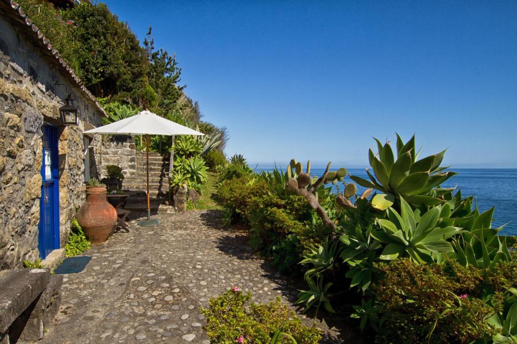 a pathway leading to a house with an umbrella and the ocean at Casa de Pedra in Ribeira Quente