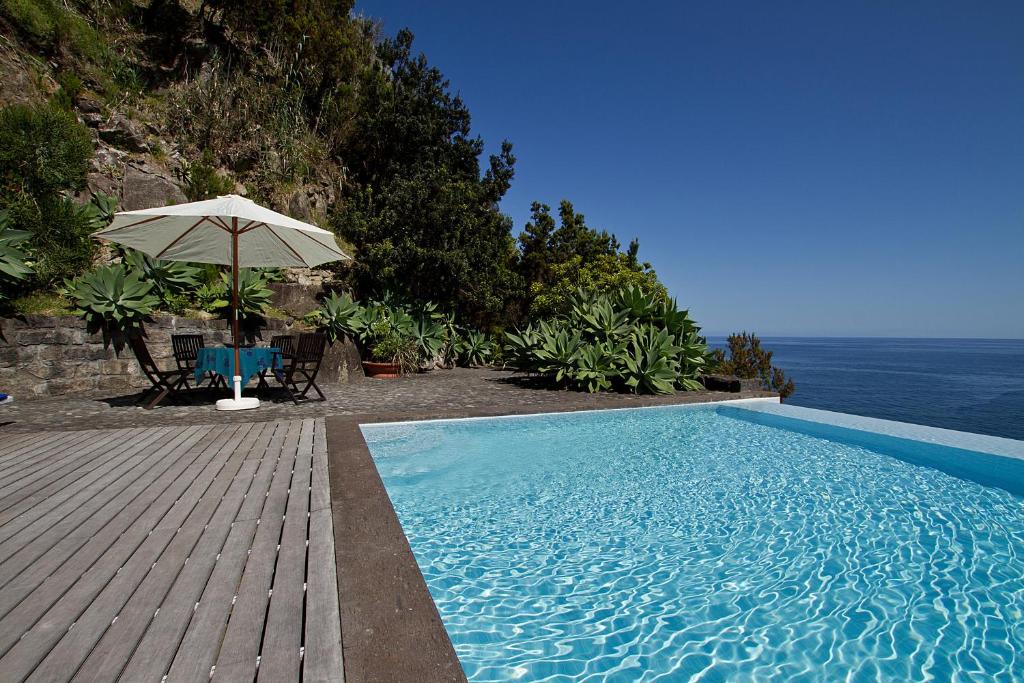 a swimming pool with an umbrella and a table and chairs at Casa de Pedra in Ribeira Quente