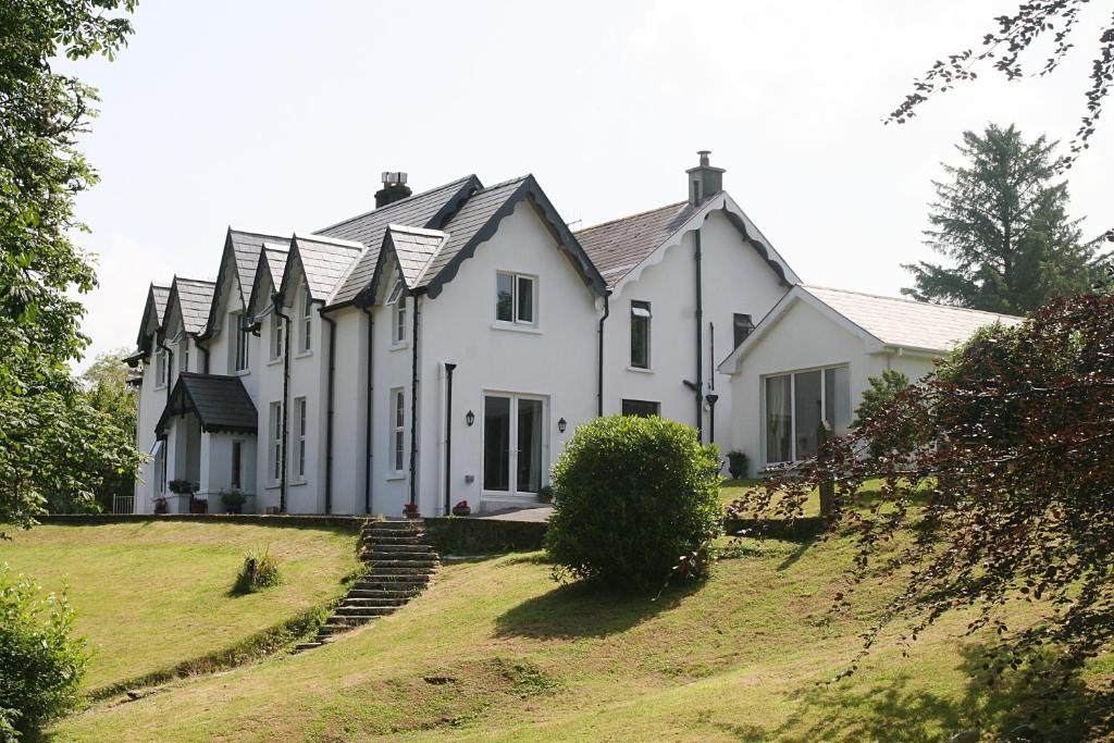 una grande casa bianca su una collina erbosa di Muxnaw Lodge a Kenmare