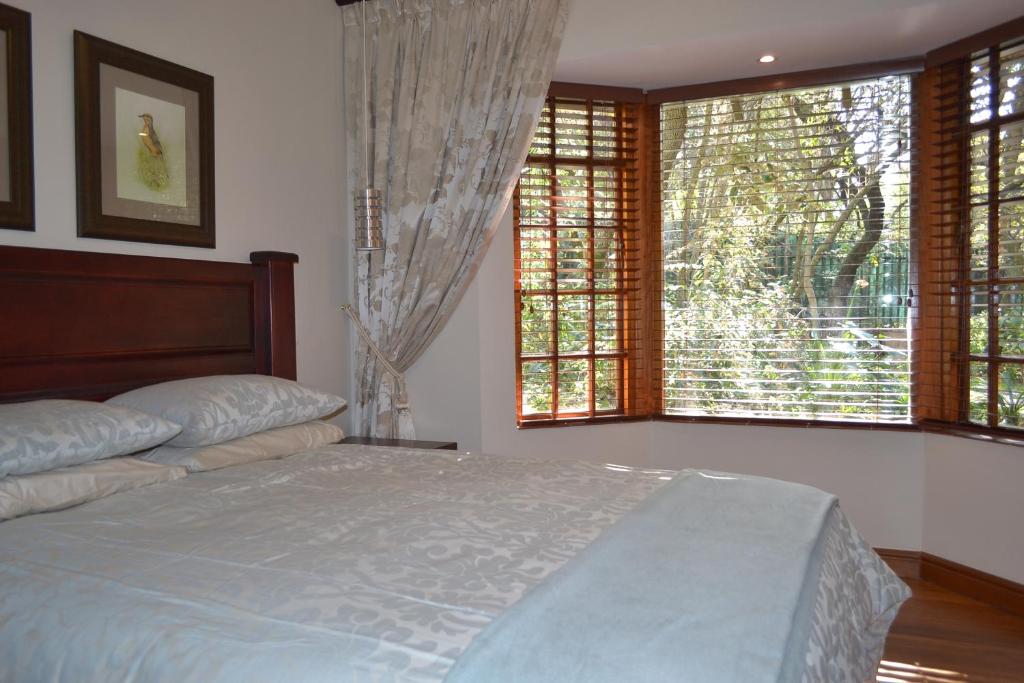 a bedroom with a bed and two large windows at Lydall Wild Tranquil Garden Suites in Johannesburg