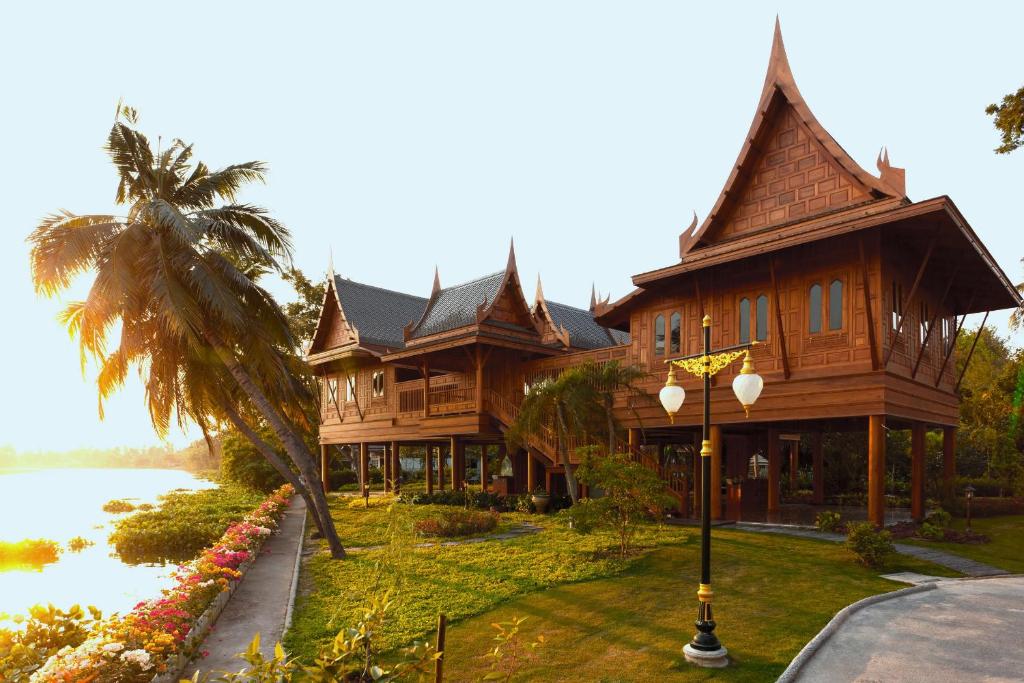 a large wooden house with a palm tree and water at RK Riverside Resort & Spa (Reon Kruewal) in Ban Khlong Krang