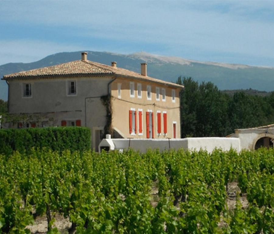 a building with red windows in front of a vineyard at Le Temps d'un Rêve in Mazan