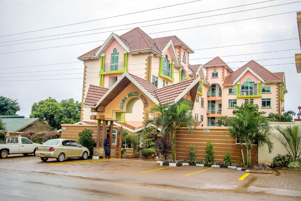 ein großes rosa und gelbes Haus mit Autos auf einem Parkplatz in der Unterkunft Casa Miltu Hotel in Kampala
