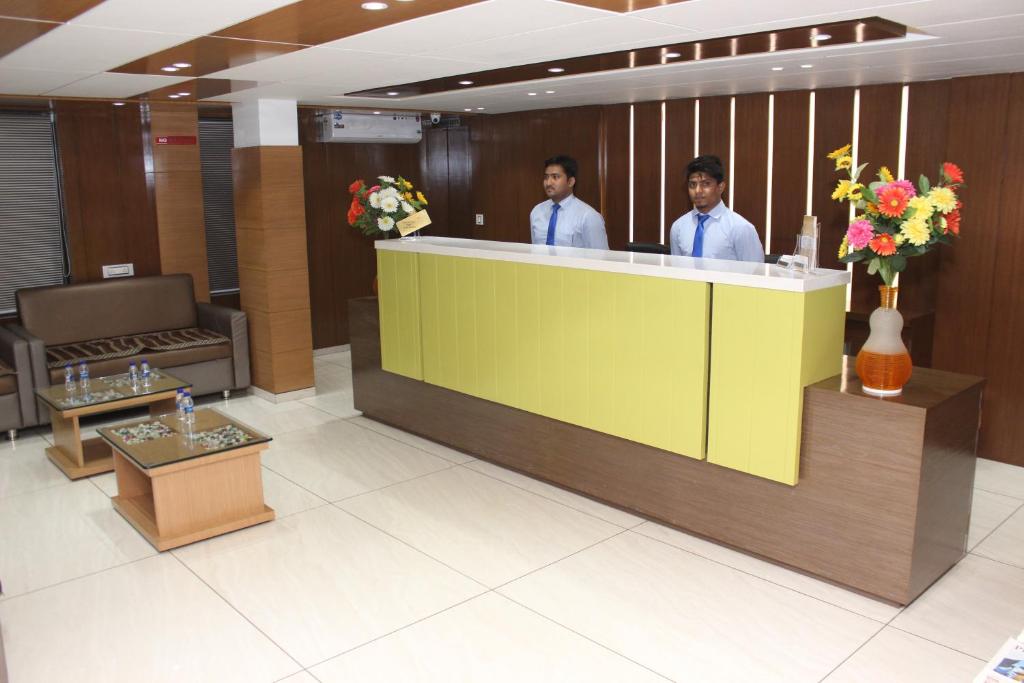 two men standing behind a counter in a lobby at Hotel The Furat Inn in Vapi