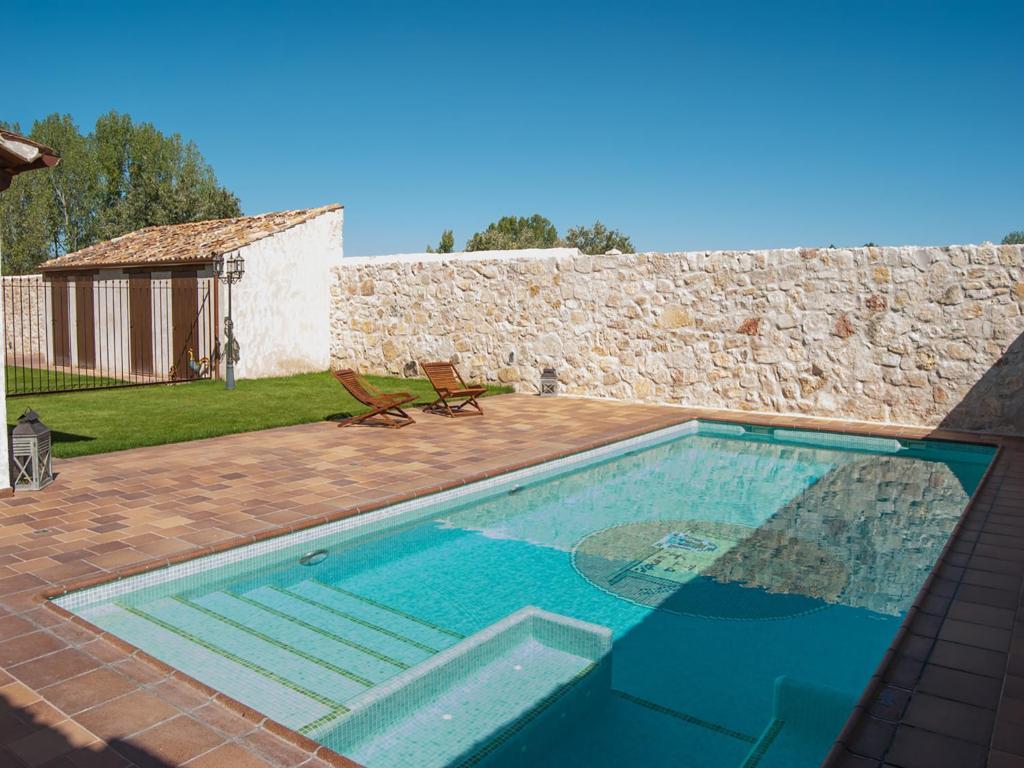 una piscina en un patio con una pared de piedra en La Fuente del Pinar, en Valdesimonte