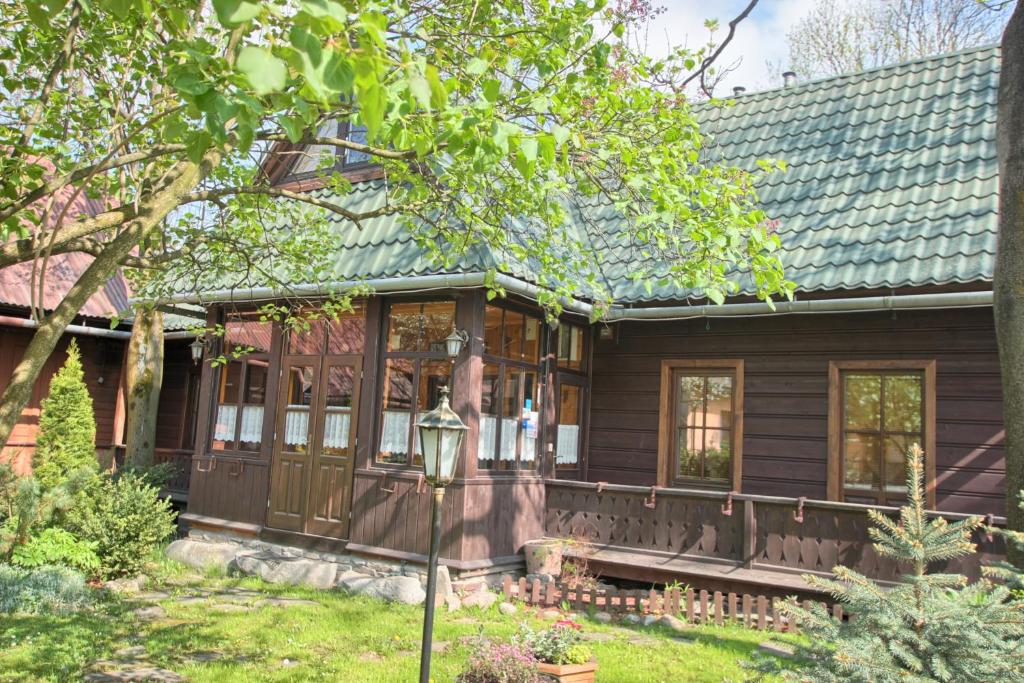a wooden house with a porch and a tree at Pokoje Gościnne Za Wnukiem in Zakopane