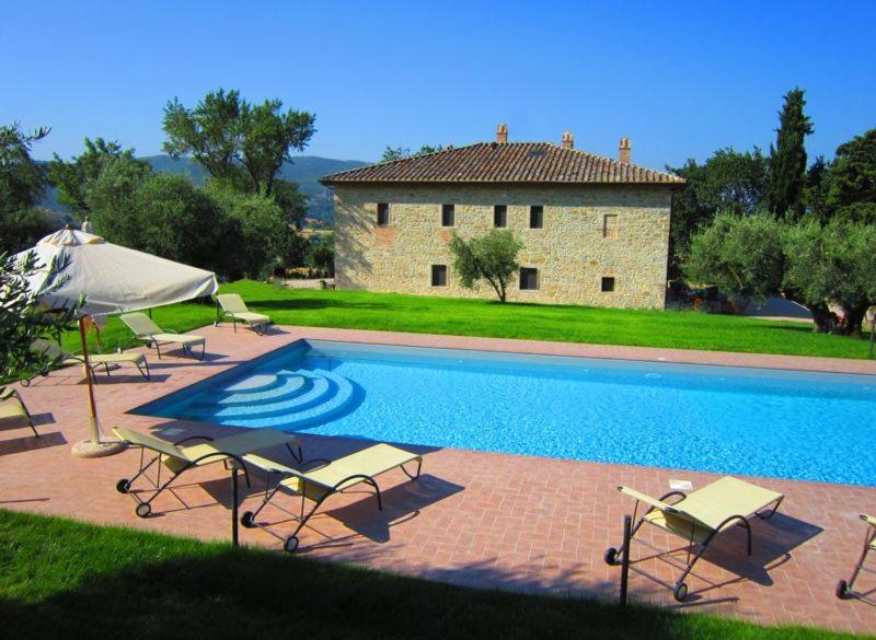 a pool with chairs and an umbrella and a building at Casale dei Dotti in Colle Umberto