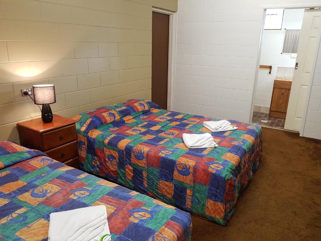 a room with two beds and a table with a lamp at Commercial Hotel in Charters Towers