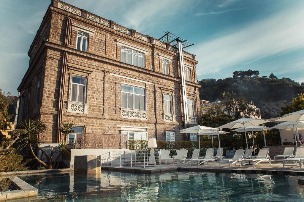 un edificio con sillas y sombrillas junto a una piscina en Artis Domus Relais & Spa en Sorrento