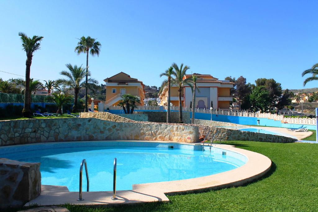 a swimming pool in a yard with palm trees and houses at Aparthotel Bahia Pinosol in Jávea
