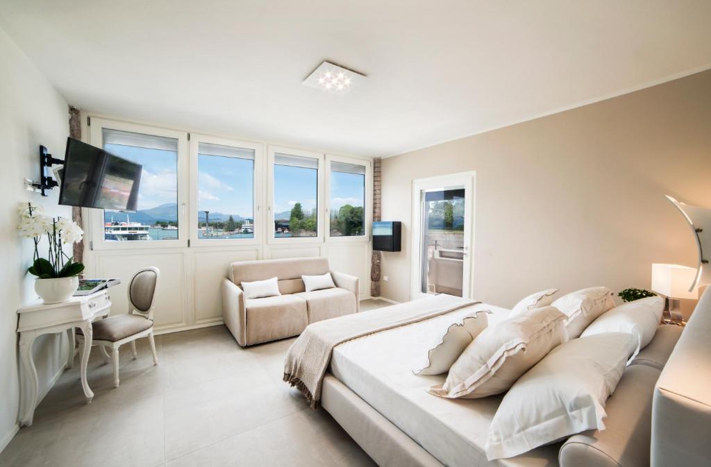 a white bedroom with a large bed and a chair at Riviera Carducci Rooms in Peschiera del Garda