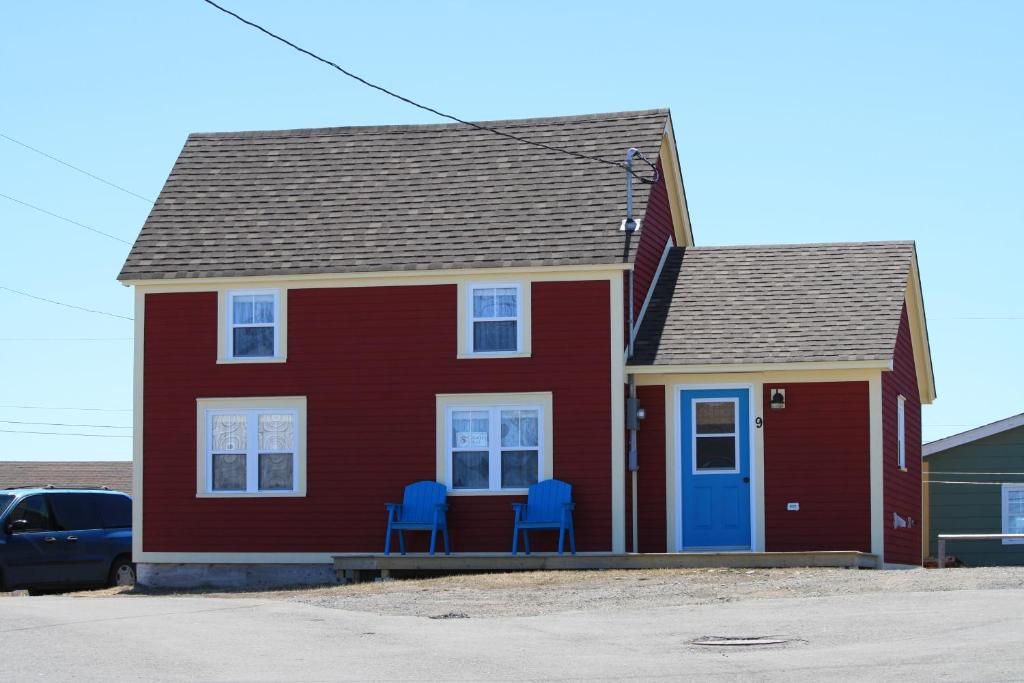 a red house with two blue chairs in front of it at Seakissed Cottage in Bonavista